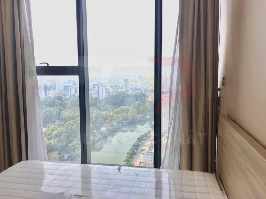 Phòng ngủ căn hộ với giường cạnh cửa sổ kính lớn nhìn ra công viên và hồ nước trong thành phố