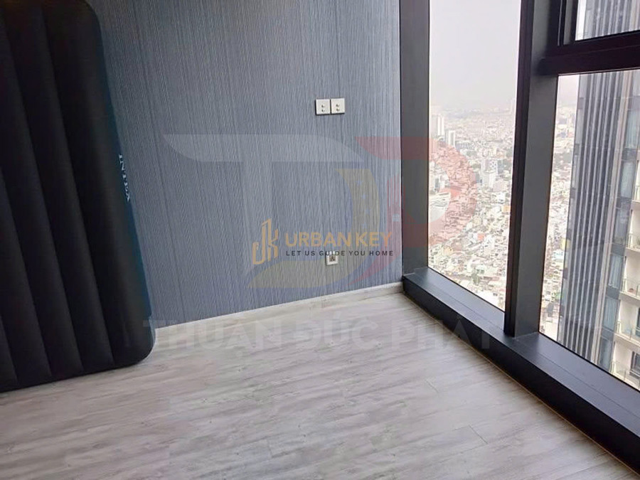 Căn phòng trống với sàn gỗ, nệm hơi sát tường và cửa sổ kính lớn nhìn ra thành phố