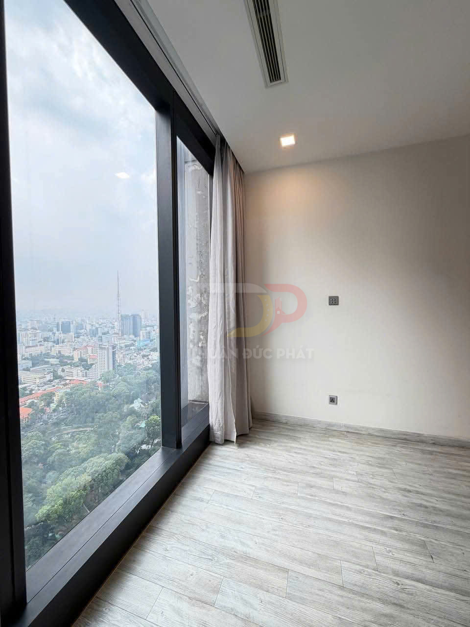 Căn hộ trống với cửa kính lớn sát sàn, rèm xám và sàn gỗ sáng nhìn ra thành phố