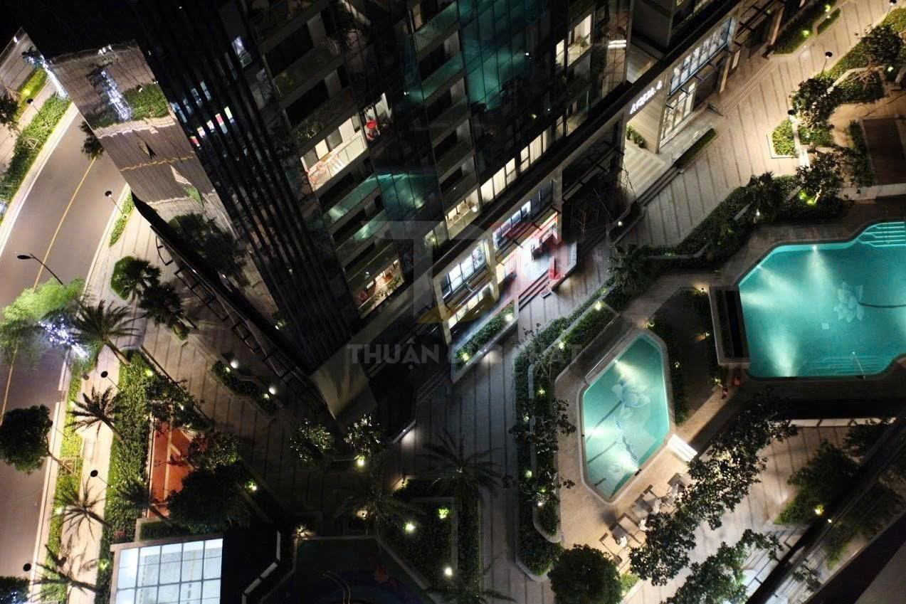 Hồ bơi ngoài trời tại khu căn hộ cao cấp nhìn từ trên cao vào ban đêm, xung quanh là cây xanh và đèn sáng