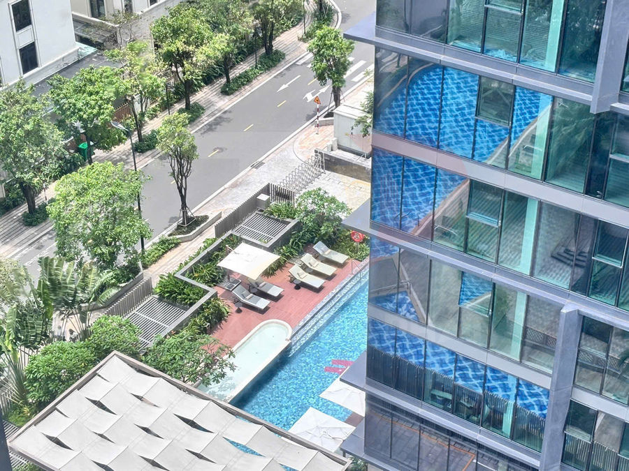Hồ bơi ngoài trời tại khu căn hộ cao tầng với ghế tắm nắng và cây xanh xung quanh