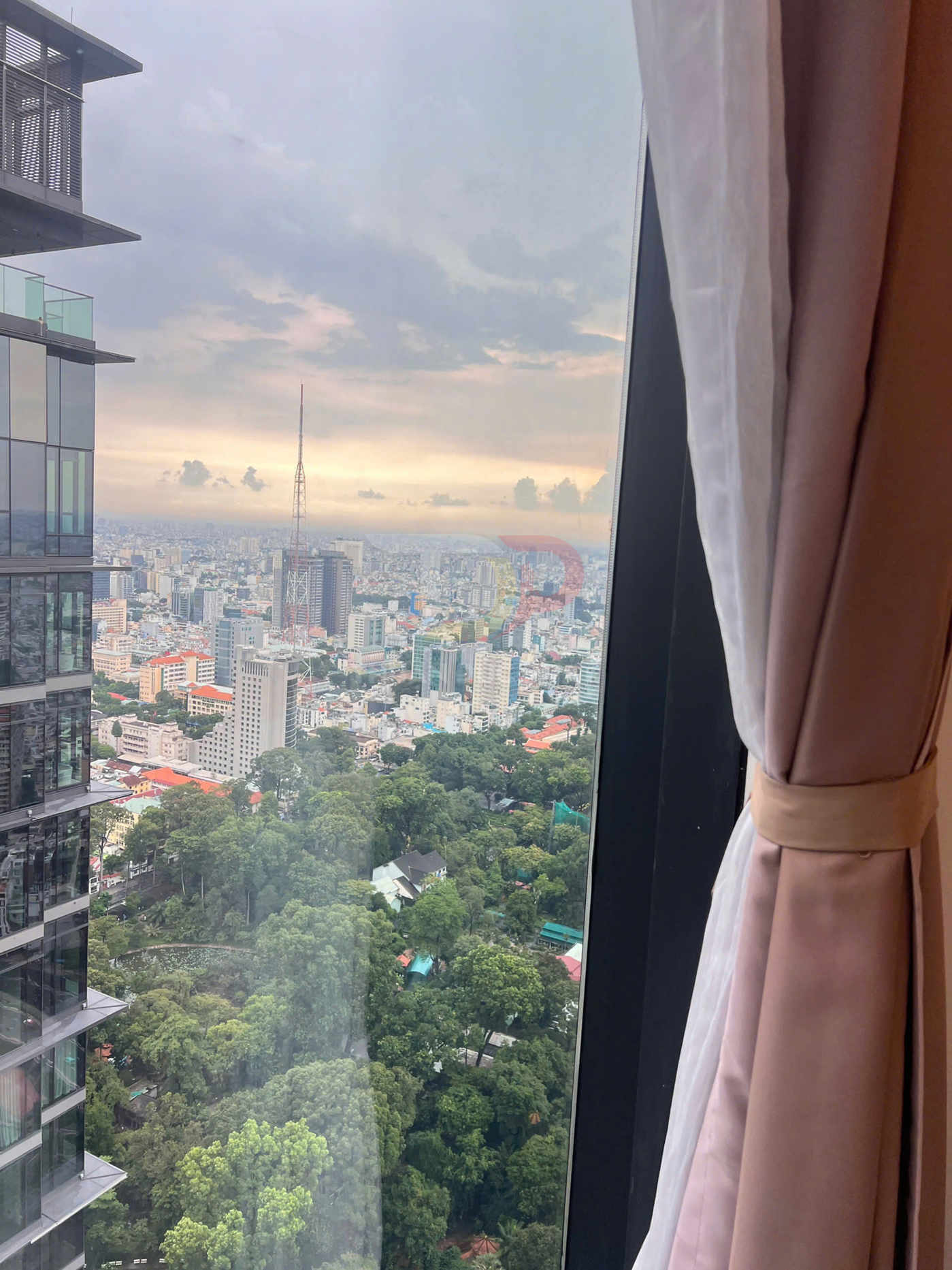 Rèm cửa màu hồng kem buộc gọn bên cửa sổ kính lớn nhìn ra thành phố và công viên nhiều cây xanh
