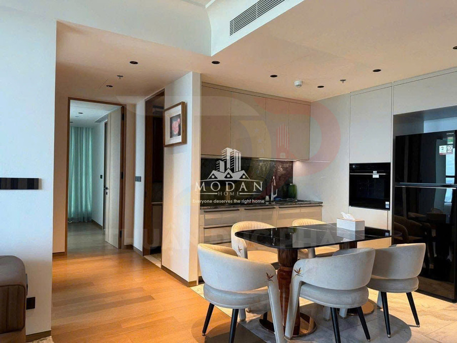 Phòng bếp hiện đại với tủ bếp màu sáng, tủ lạnh đen và bàn ăn kính cùng ghế bọc nệm