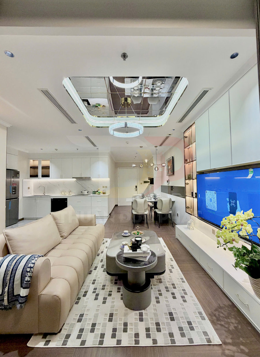 Phòng khách căn hộ hiện đại với sofa da màu be, bàn trà đôi, thảm họa tiết và tủ kệ tivi liền bếp mở rộng