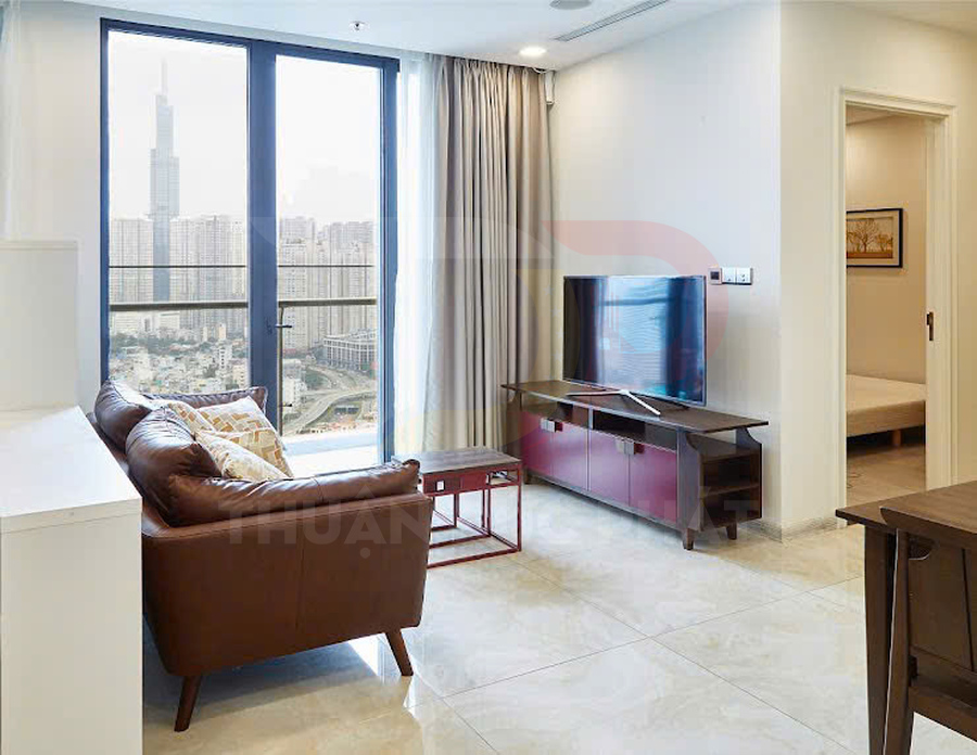 Phòng khách căn hộ hiện đại với sofa da nâu, bàn trà, kệ tivi gỗ và cửa kính lớn nhìn ra thành phố