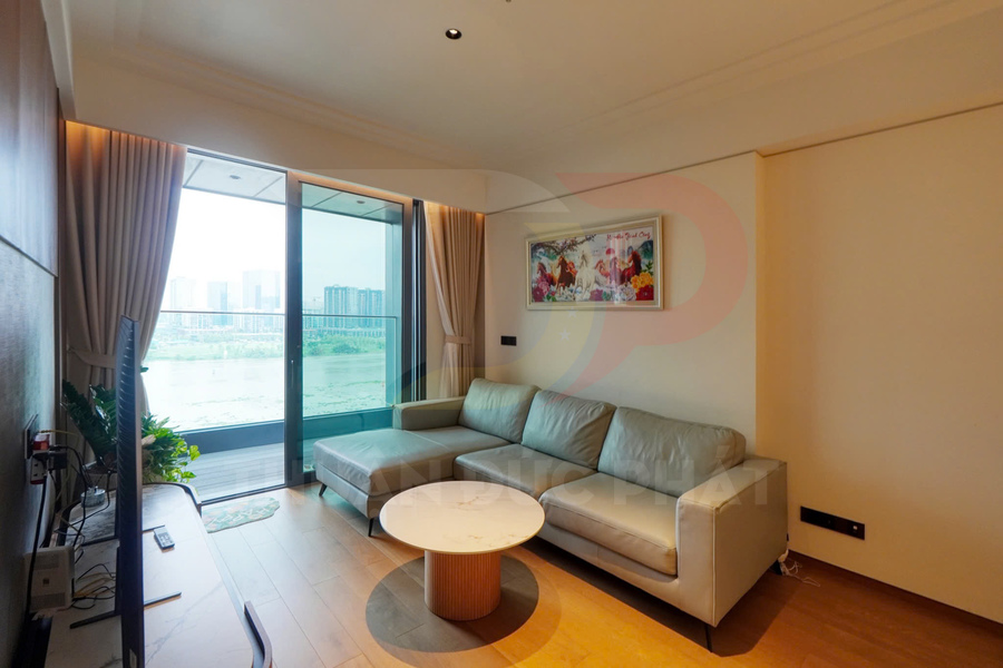 Phòng khách chung cư hiện đại với sofa góc da màu kem, bàn trà tròn và cửa kính lớn nhìn ra sông