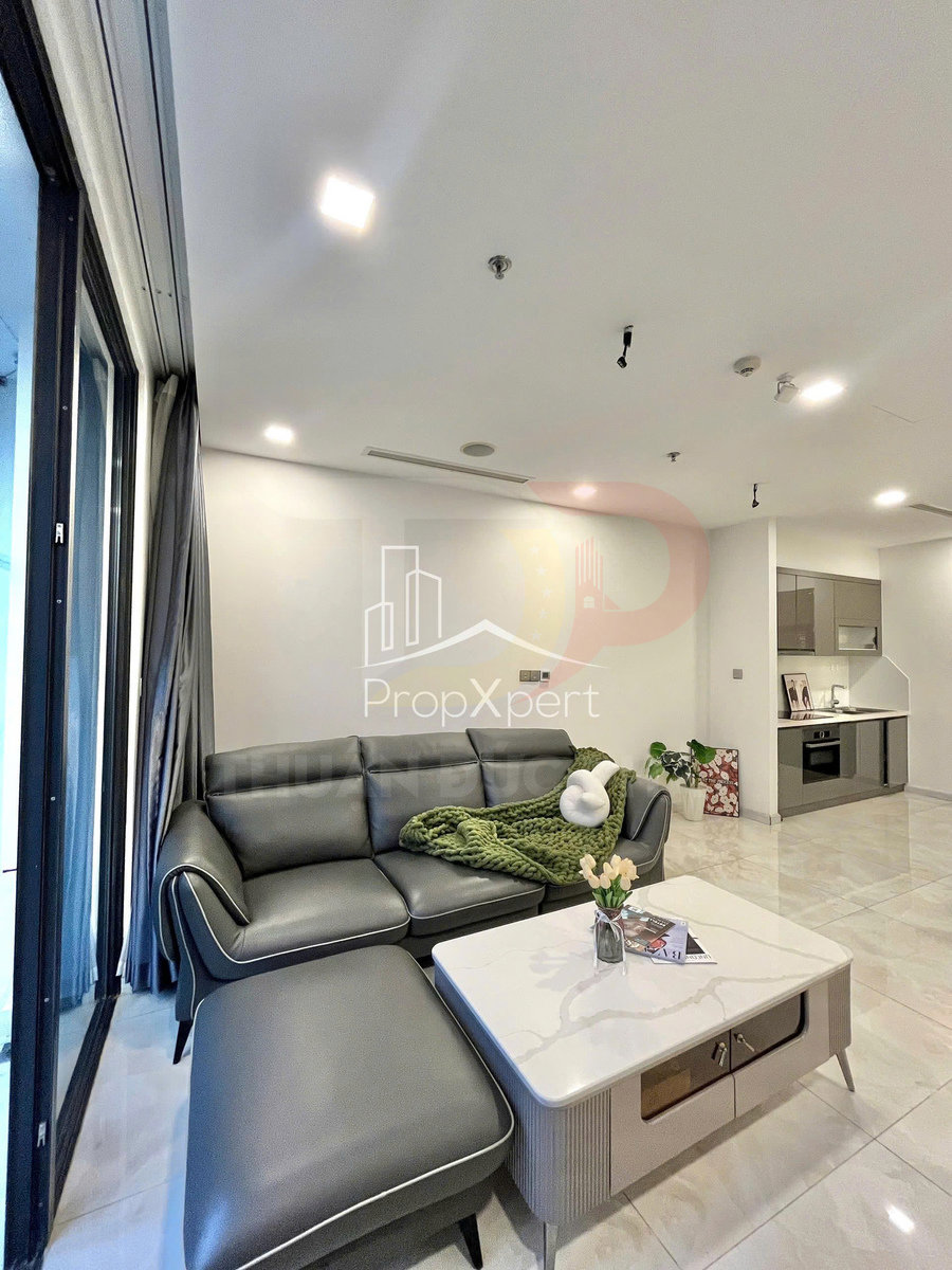 Sofa da góc màu xám hiện đại trong phòng khách chung cư, kèm bàn trà mặt đá và bếp mở liền kề