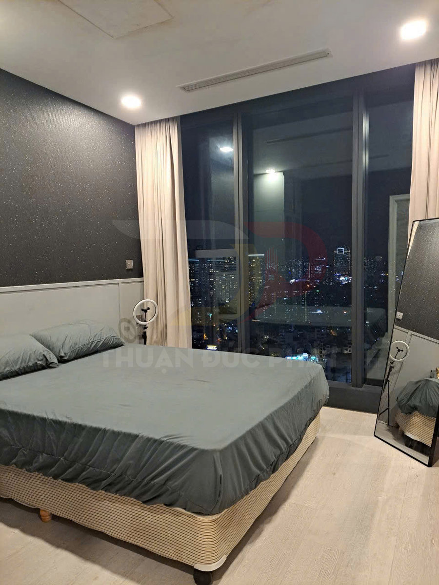 Giường ngủ bọc ga màu xám trong phòng ngủ hiện đại có cửa kính lớn nhìn ra thành phố ban đêm