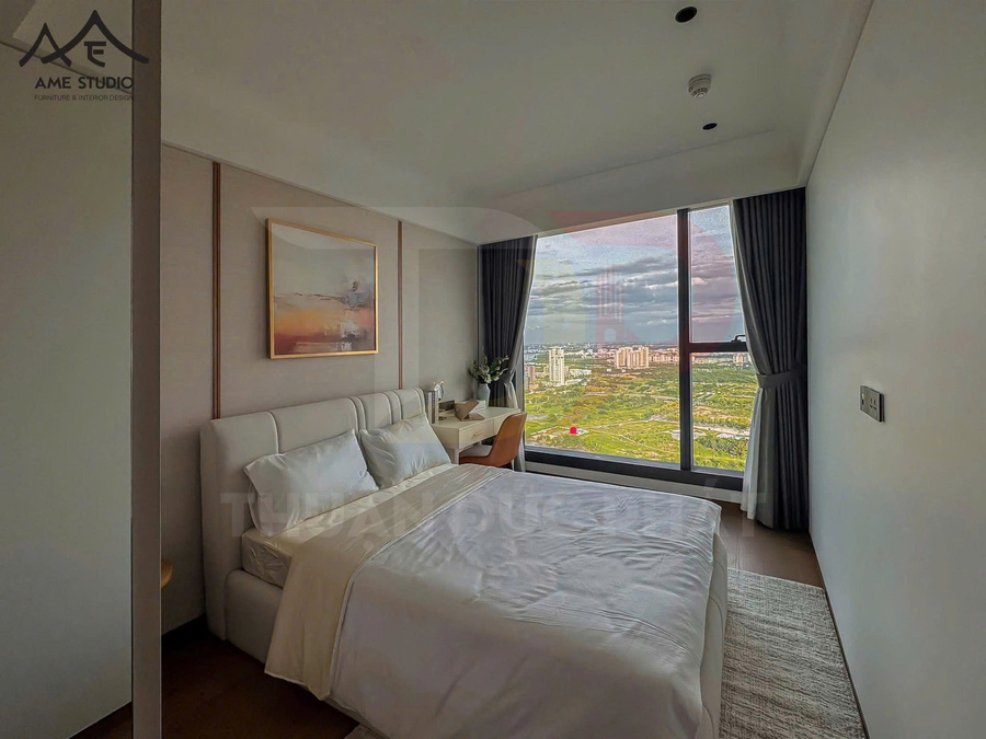 Phòng ngủ chung cư hiện đại với giường đôi bọc da trắng, bàn làm việc cạnh cửa sổ kính lớn view thành phố