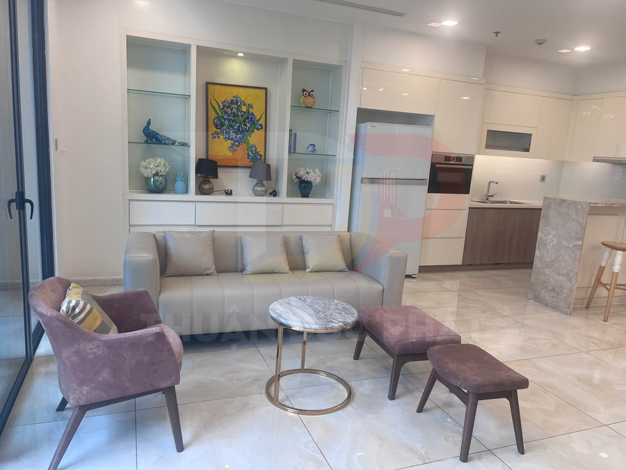 Phòng khách căn hộ hiện đại với sofa xám, bàn trà mặt đá tròn và ghế nệm cạnh bếp tích hợp tủ lạnh trắng