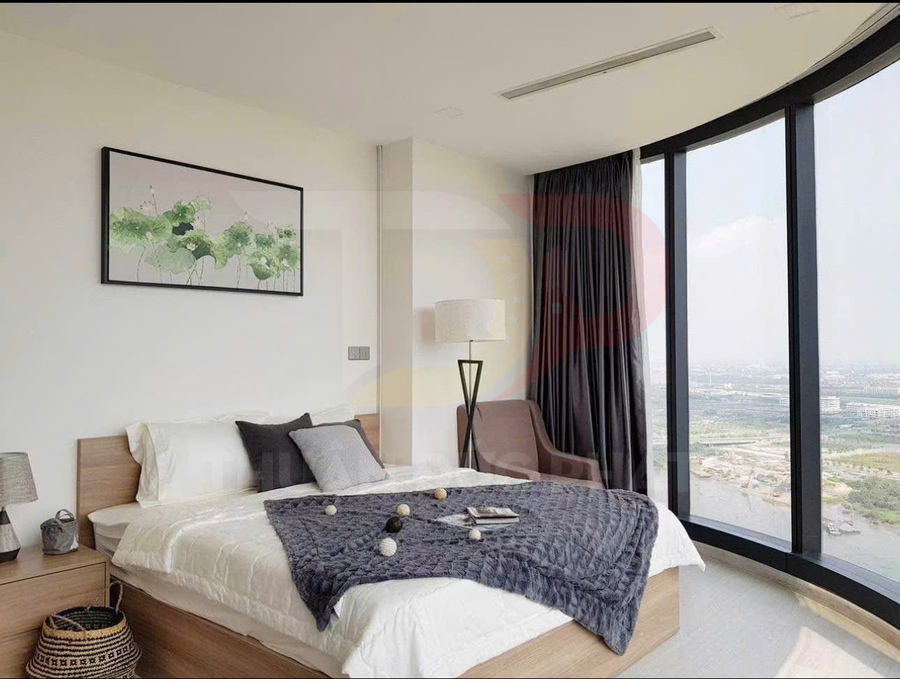 Phòng ngủ hiện đại với giường gỗ, chăn xám, ghế bành cạnh cửa kính lớn view toàn cảnh thành phố