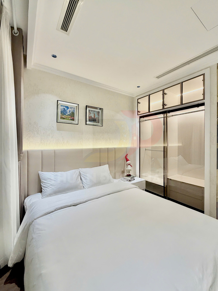 Phòng ngủ hiện đại với giường đôi ga trắng, tủ quần áo cửa kính và tranh treo tường trang trí
