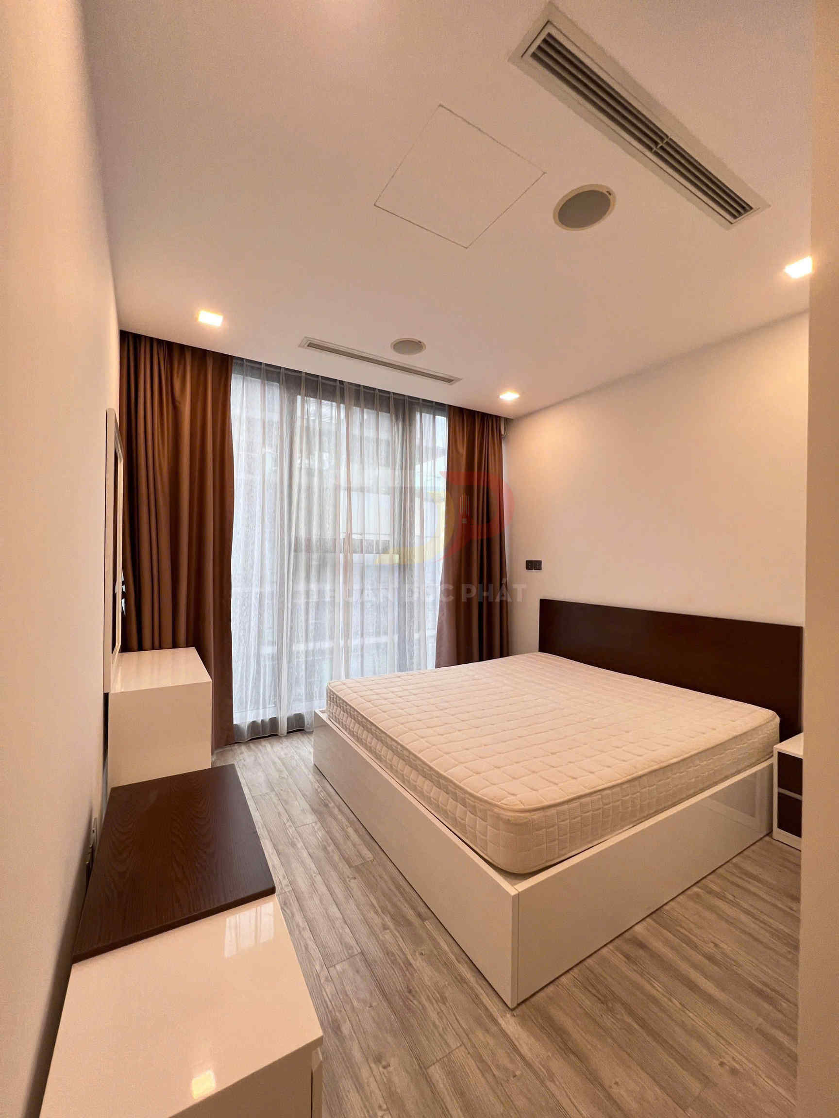 Phòng ngủ tối giản với giường ngủ gỗ màu trắng nệm dày, sàn gỗ và rèm cửa lớn màu nâu