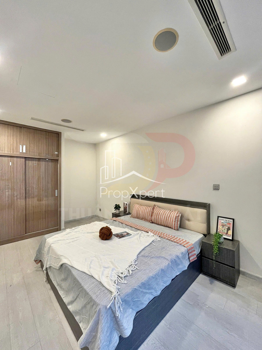 Phòng ngủ hiện đại với giường đôi trải ga xám trắng, tủ quần áo gỗ và bàn đầu giường trang trí cây xanh