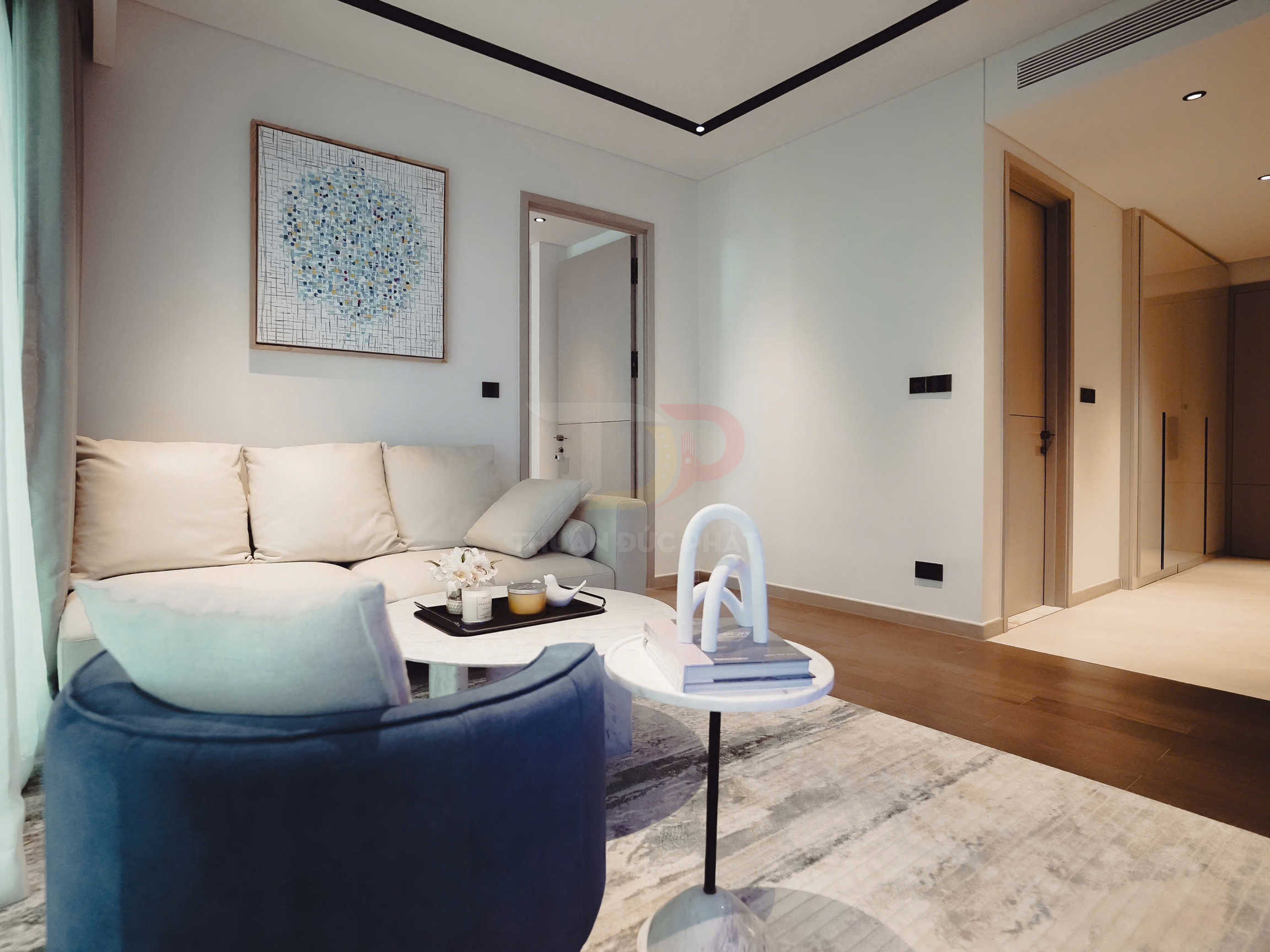 Phòng khách hiện đại với sofa vải màu kem, ghế bành xanh và bàn trà tròn trang trí nến, sách