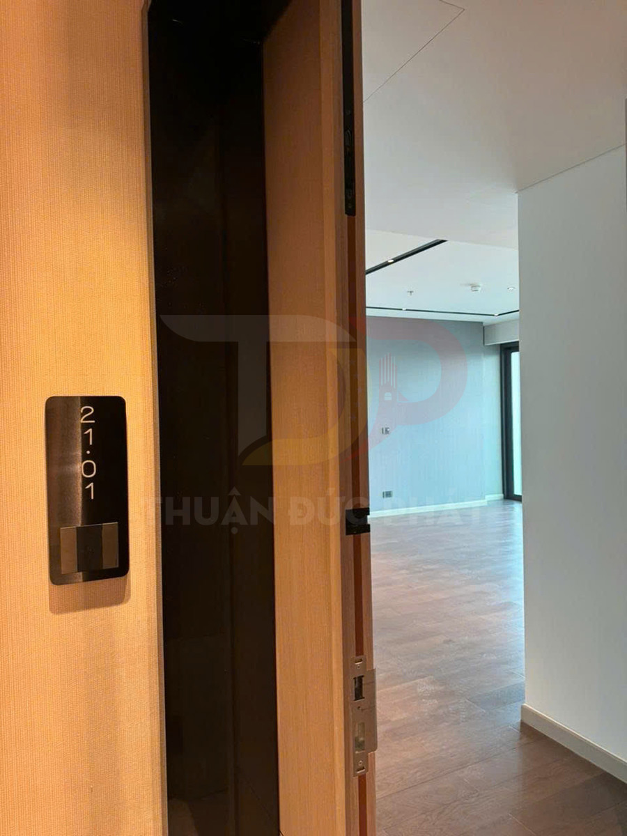 Cửa gỗ căn hộ mở vào phòng khách lát sàn gỗ, bảng số phòng 2101 gắn cạnh cửa