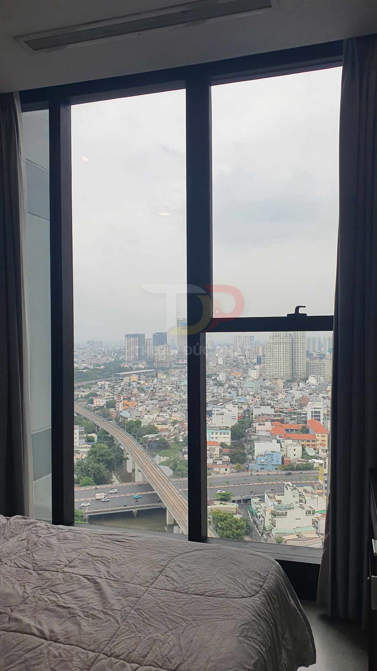 Phòng ngủ căn hộ với giường cạnh cửa sổ kính lớn nhìn ra toàn cảnh thành phố đông đúc