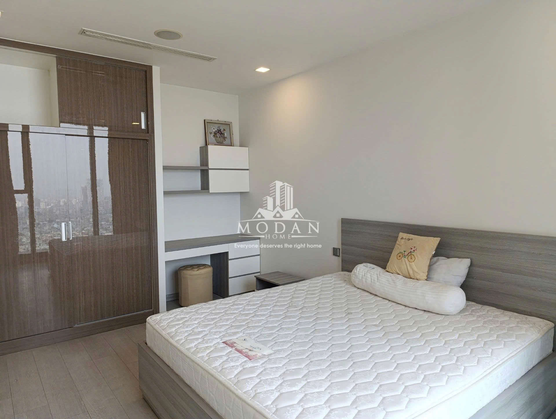 Phòng ngủ hiện đại với giường nệm trắng, tủ quần áo gỗ lớn và bàn làm việc cạnh cửa sổ rộng