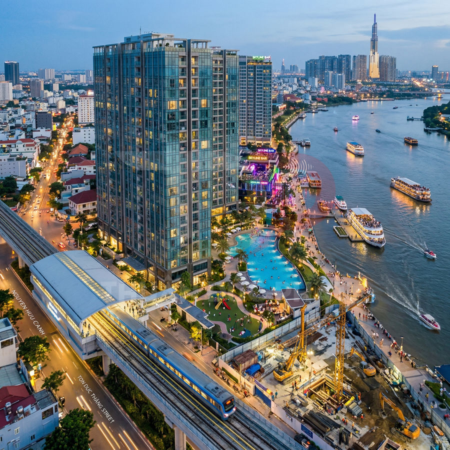 Toà nhà căn hộ cao tầng ven sông với hồ bơi ngoài trời, bến du thuyền và tuyến metro trên cao ban đêm