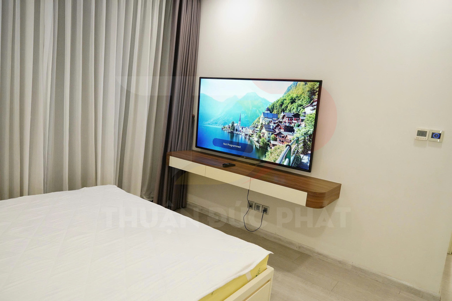 Tivi màn hình phẳng treo tường trên kệ gỗ trong phòng ngủ hiện đại có giường và rèm cửa