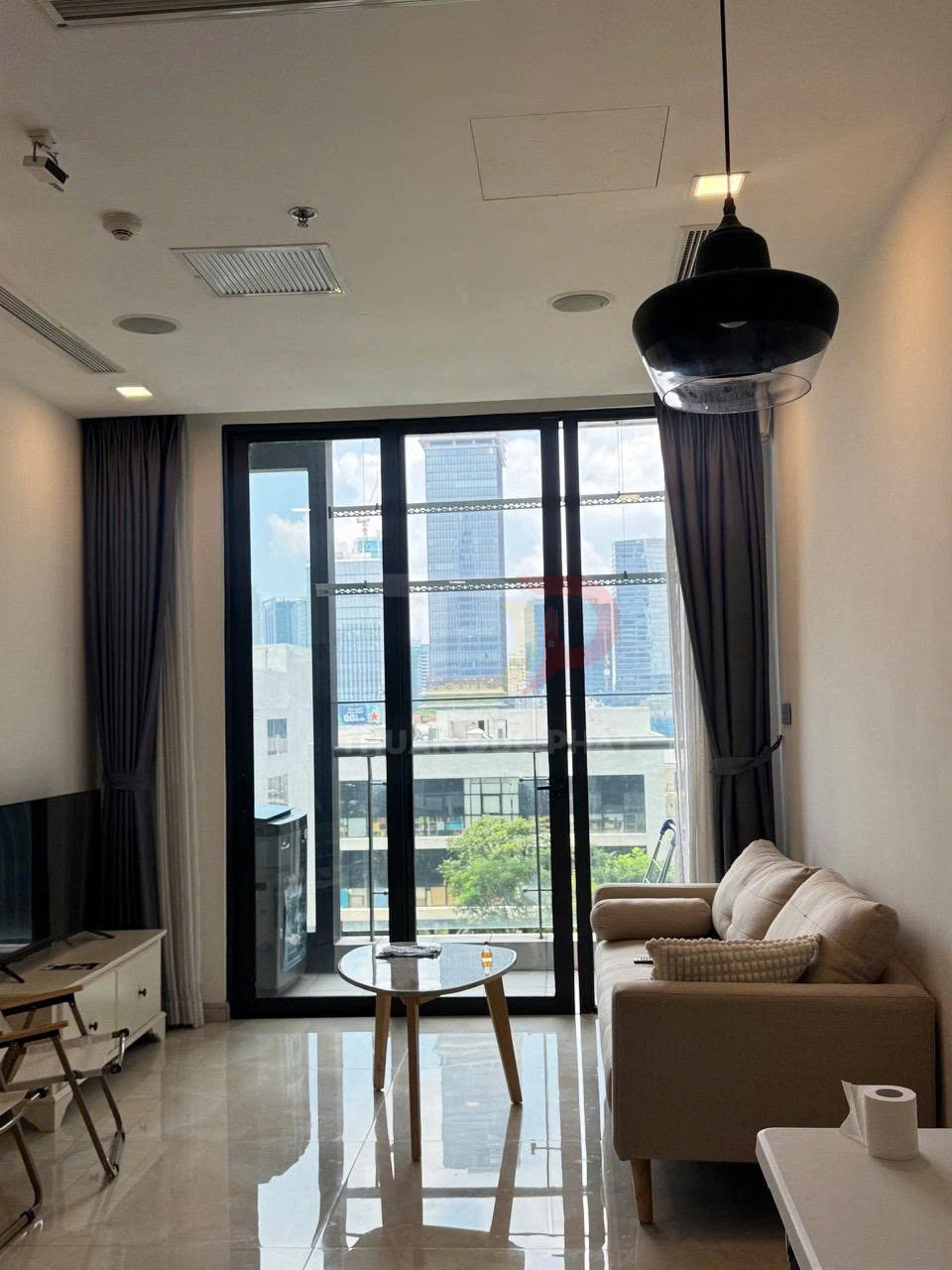 Phòng khách căn hộ hiện đại với sofa màu be, bàn trà gỗ và cửa kính lớn nhìn ra thành phố