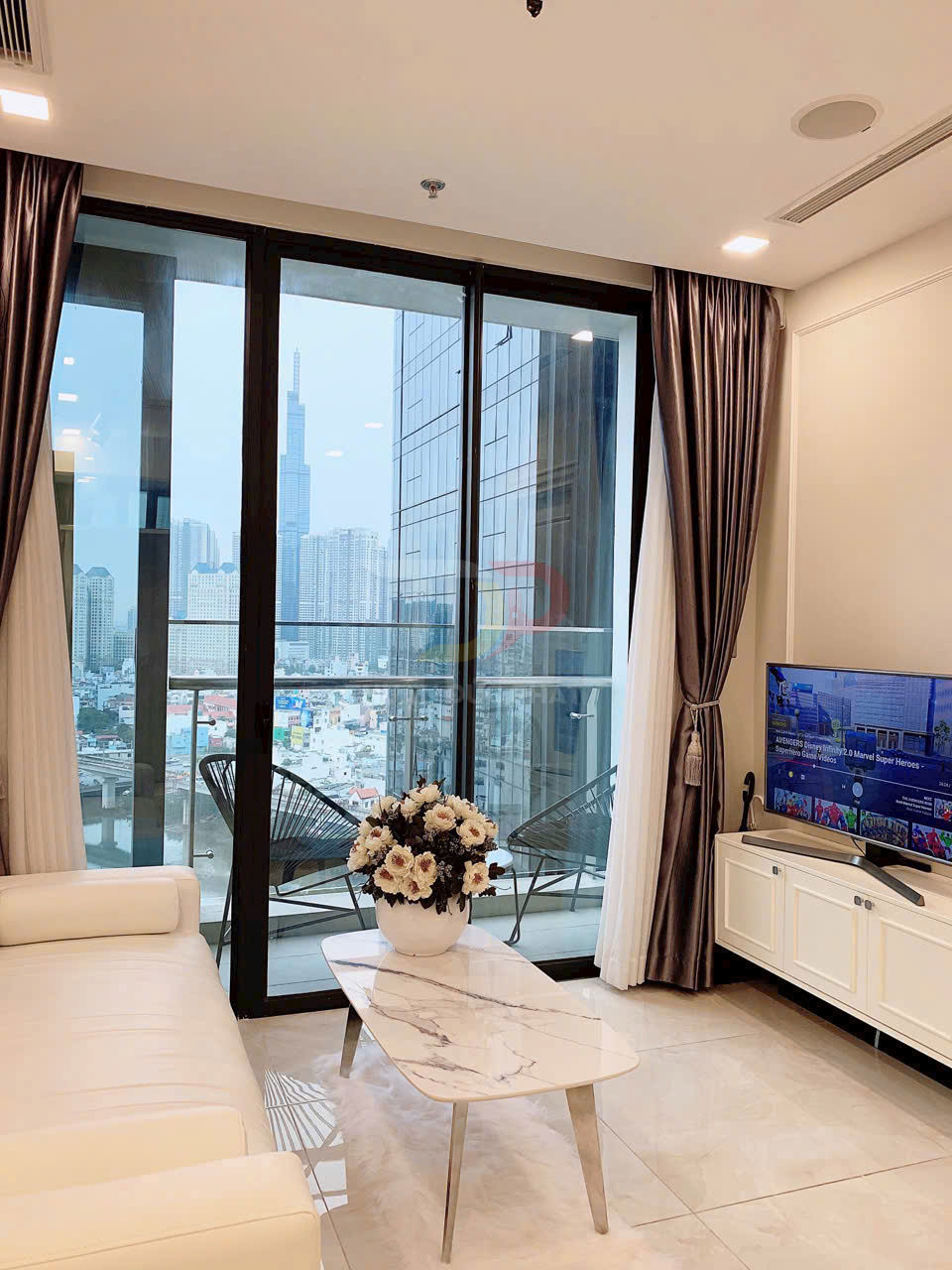 Phòng khách chung cư hiện đại với sofa trắng, bàn trà đá hoa cương và tivi cạnh cửa kính lớn nhìn ra thành phố
