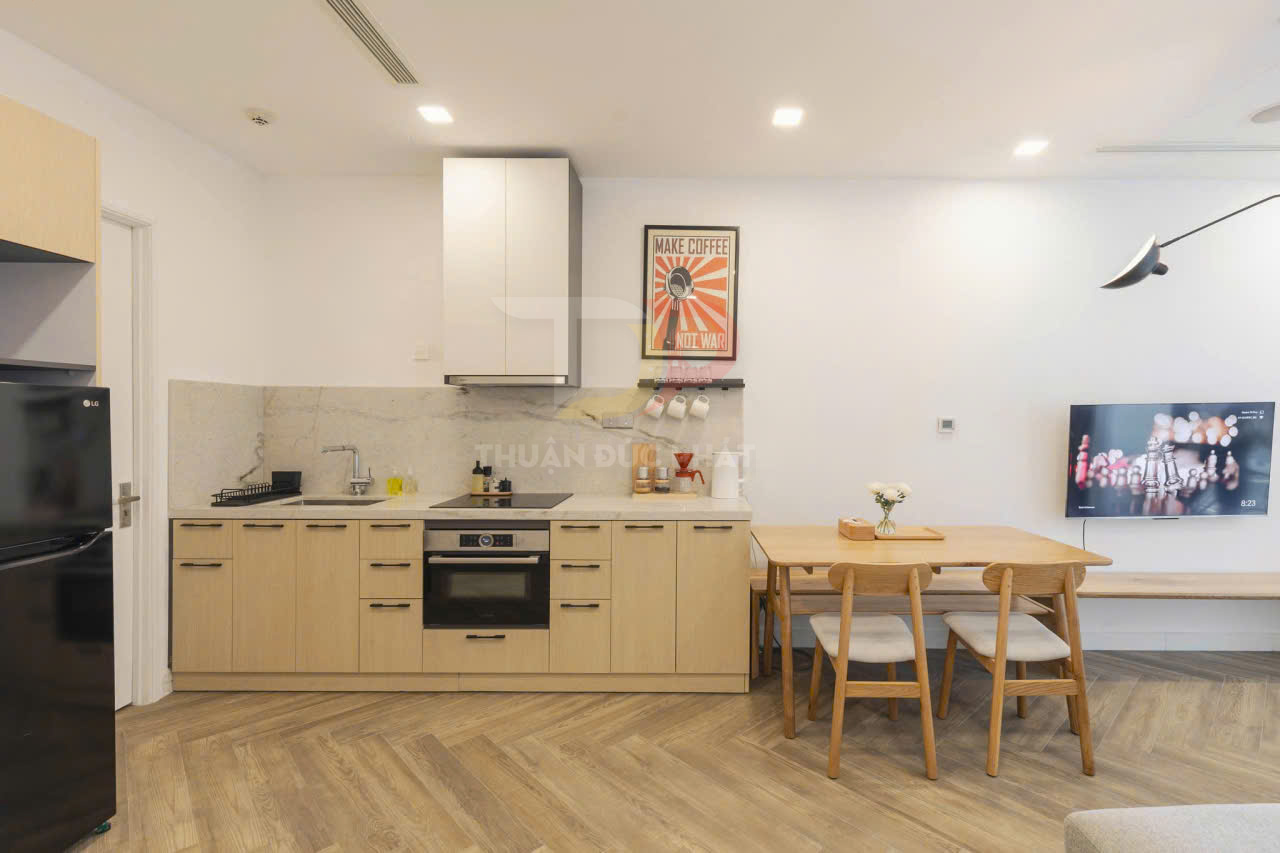 Tủ bếp gỗ hiện đại với bếp từ, lò nướng âm tủ và bàn ăn gỗ nhỏ trong căn hộ sáng sủa