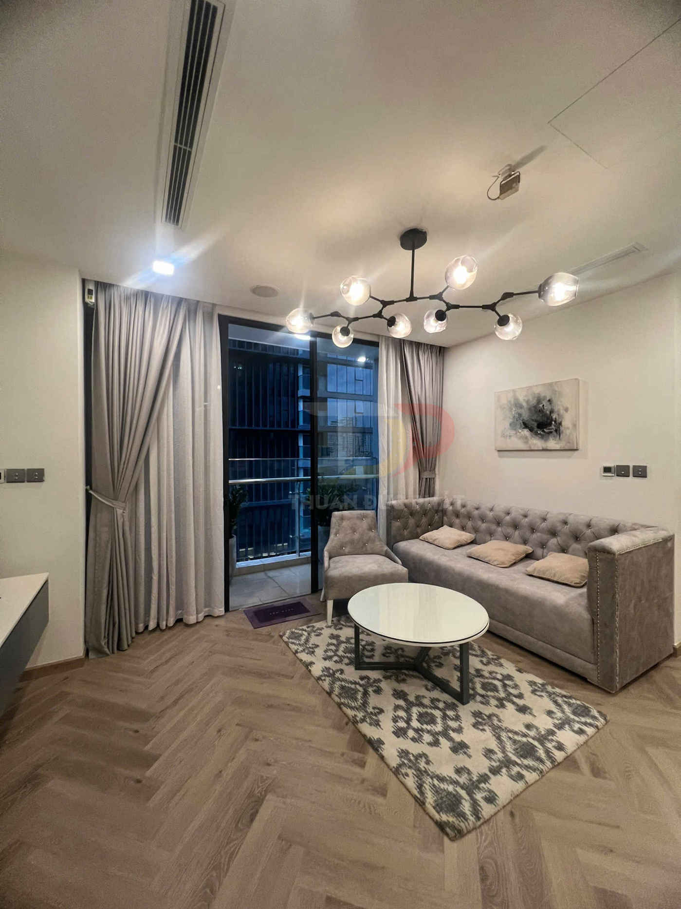 Phòng khách chung cư hiện đại với sofa bọc nhung màu xám, bàn trà tròn và đèn trần trang trí nhiều bóng