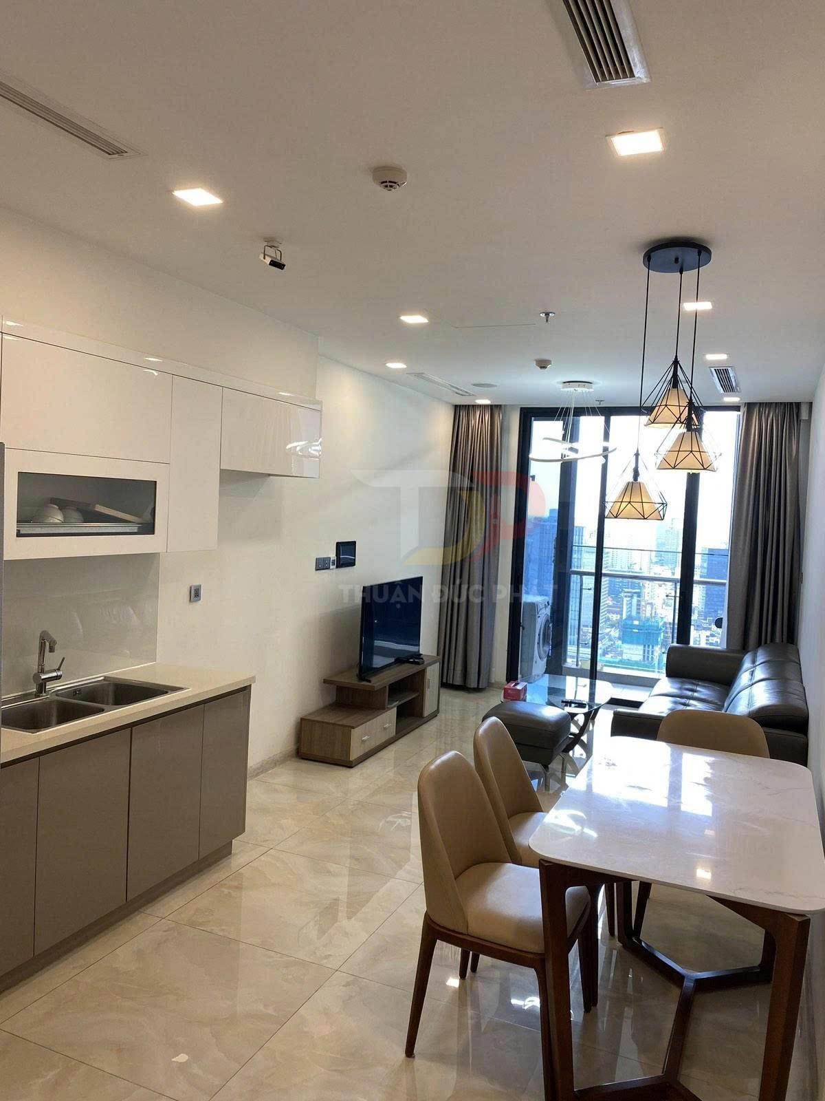 Căn hộ chung cư hiện đại với bếp liền phòng khách, bàn ăn, sofa da và cửa kính lớn nhìn ra ban công