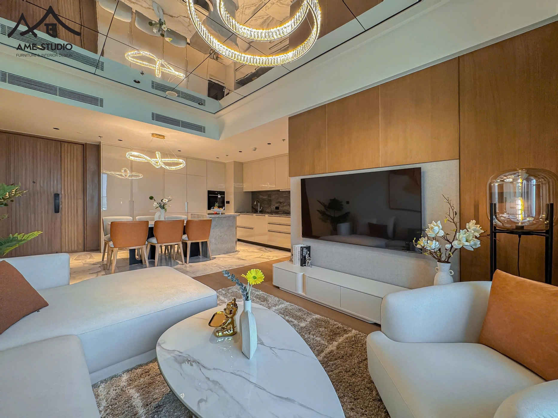 Phòng khách hiện đại với sofa sáng màu, bàn trà đá, tivi treo tường lớn liền kề bếp và bàn ăn sang trọng