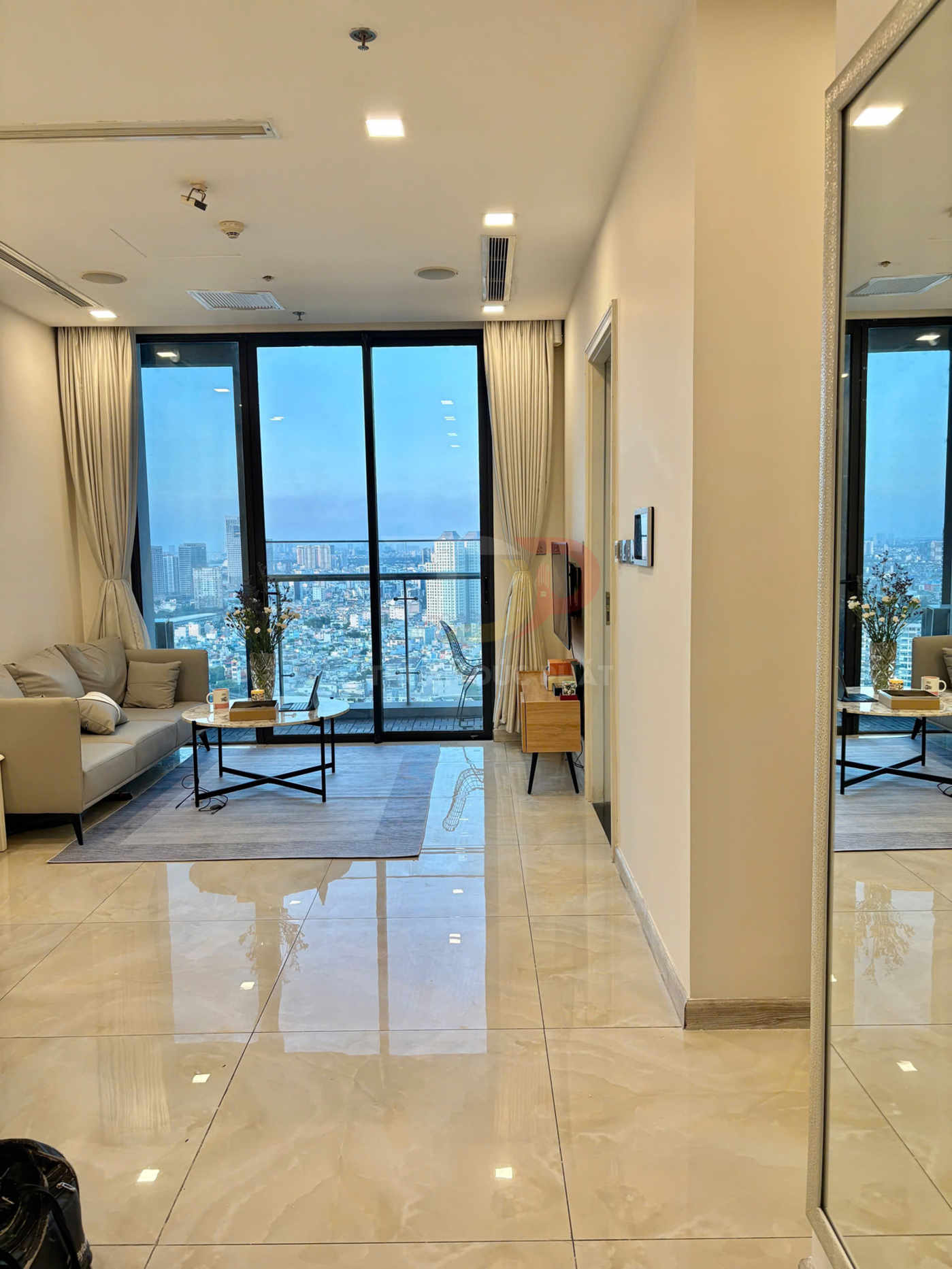 Phòng khách chung cư hiện đại với sofa, bàn trà, sàn gạch bóng và cửa kính lớn nhìn ra thành phố