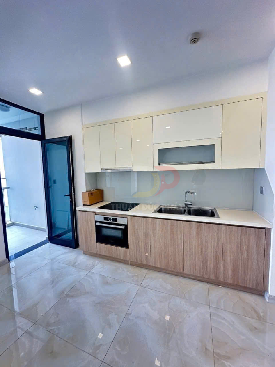 Tủ bếp gỗ hiện đại kèm bếp âm và chậu rửa đôi trong căn hộ sáng sủa có cửa kính ra ban công