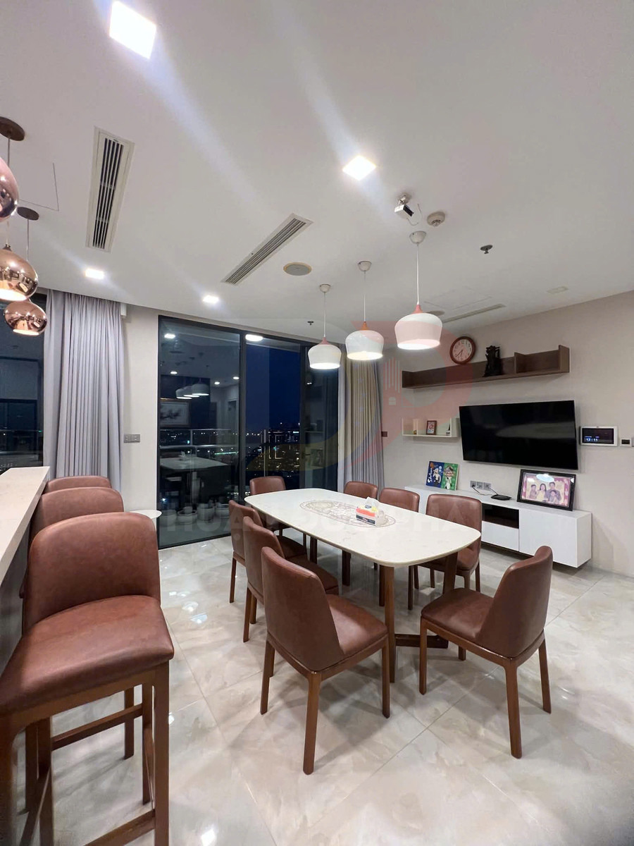 Bộ bàn ăn mặt đá với ghế da nâu trong phòng ăn chung cư hiện đại, cạnh quầy bar và cửa kính lớn