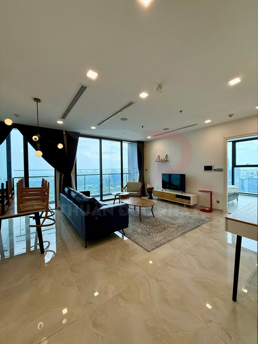 Phòng khách căn hộ cao cấp với sofa da, bàn trà gỗ, tivi treo tường và cửa kính lớn view thành phố