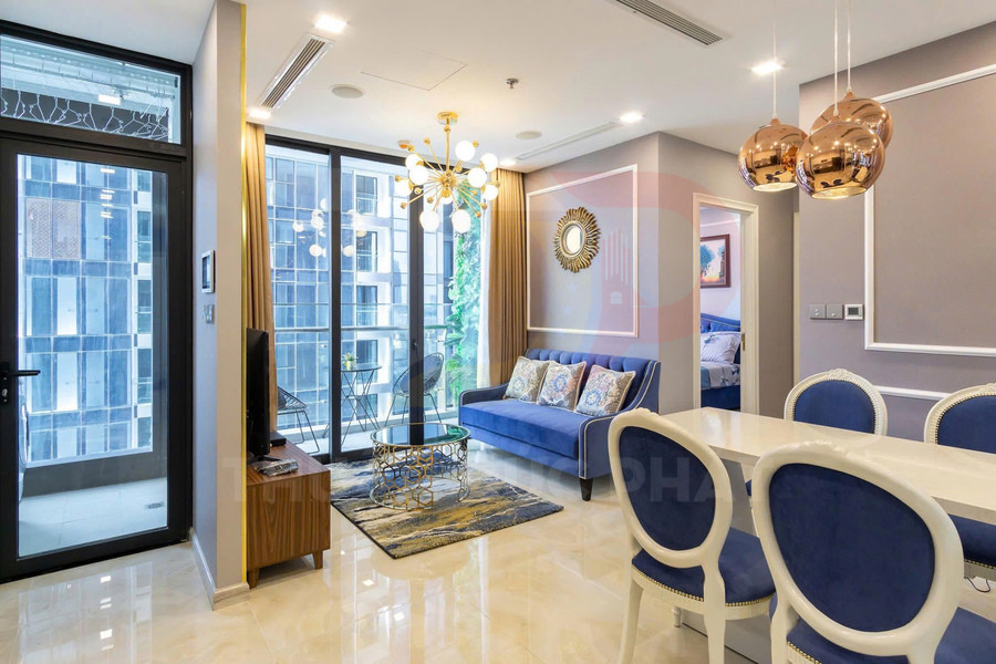 Phòng khách căn hộ hiện đại với sofa xanh, bàn trà kính, đèn chùm vàng và bàn ăn ghế bọc nệm xanh