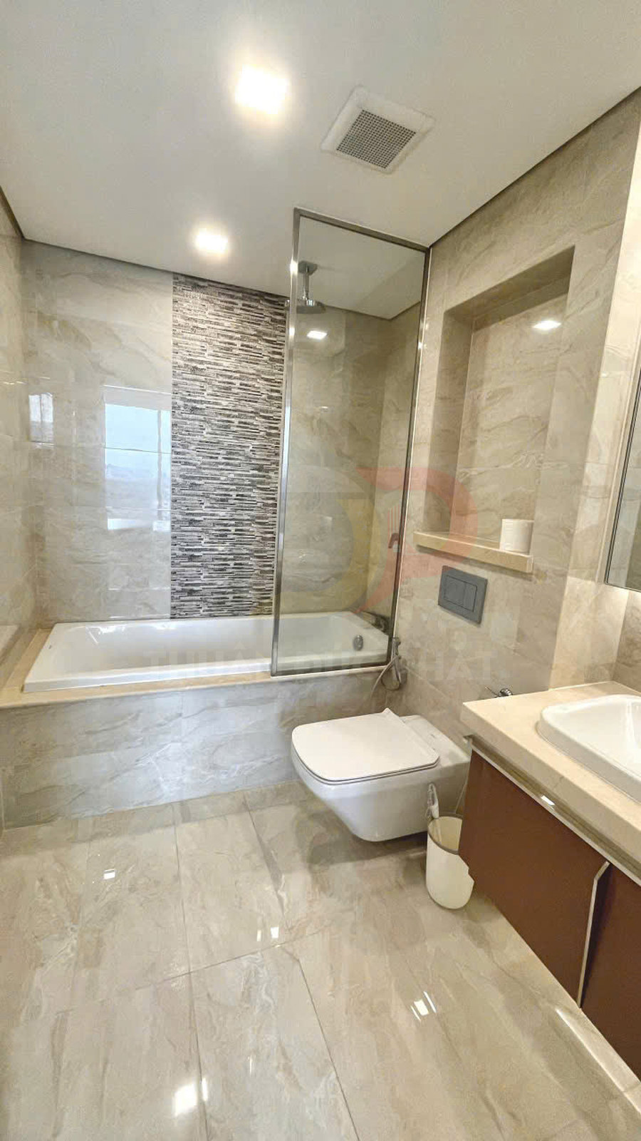 Phòng tắm hiện đại với bồn tắm kính, bồn cầu treo tường và lavabo trên tủ gỗ, ốp gạch đá sáng