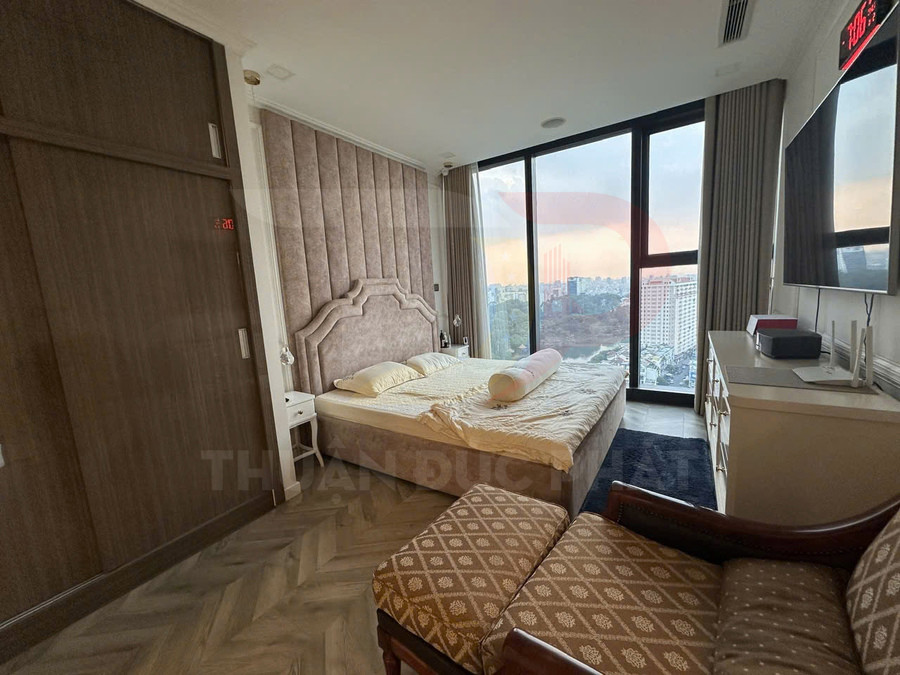 Phòng ngủ chung cư cao cấp với giường đôi bọc nệm, cửa kính lớn view thành phố lúc hoàng hôn
