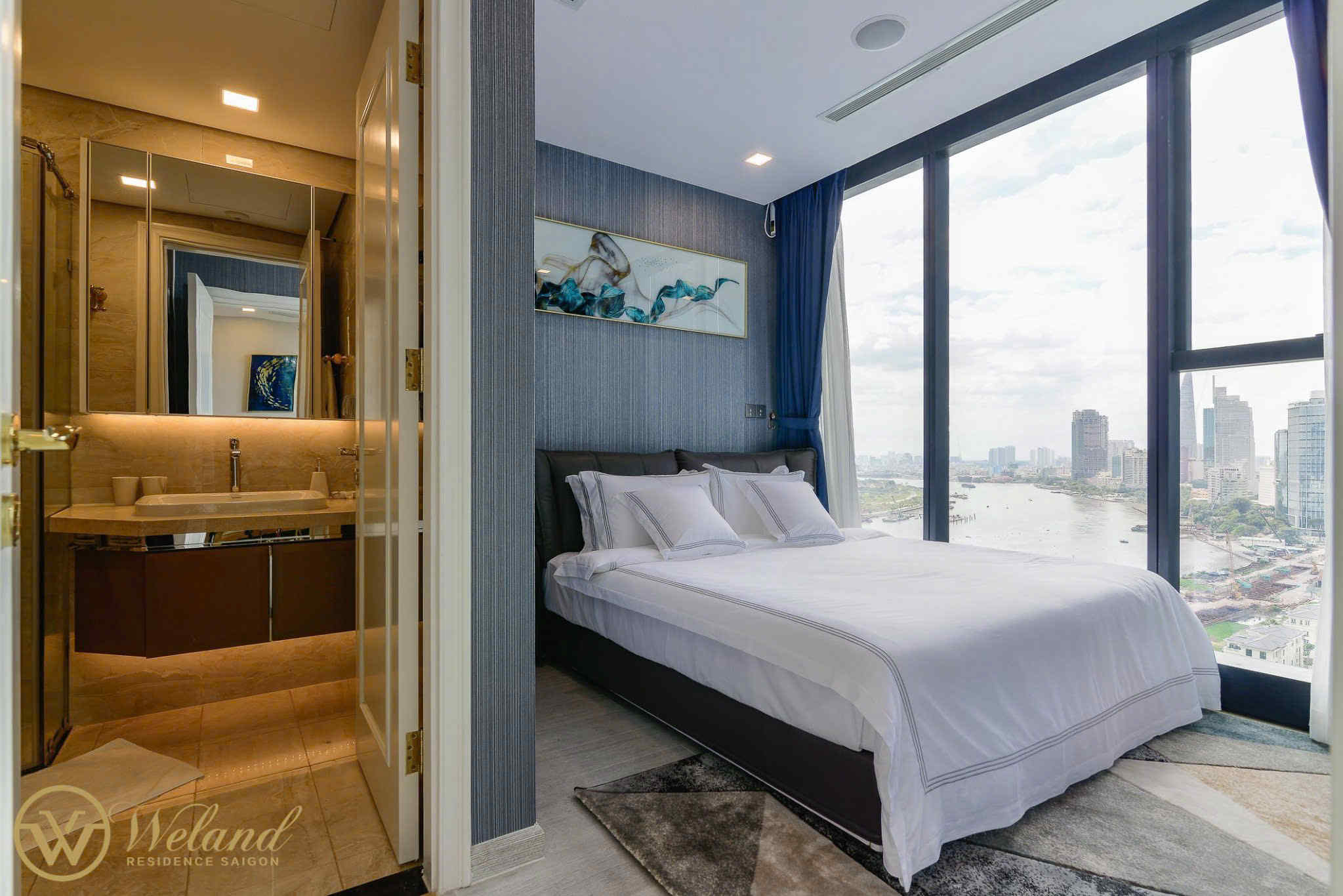 Phòng ngủ căn hộ cao cấp với giường đôi trắng, cửa sổ kính lớn view sông và phòng tắm khép kín hiện đại