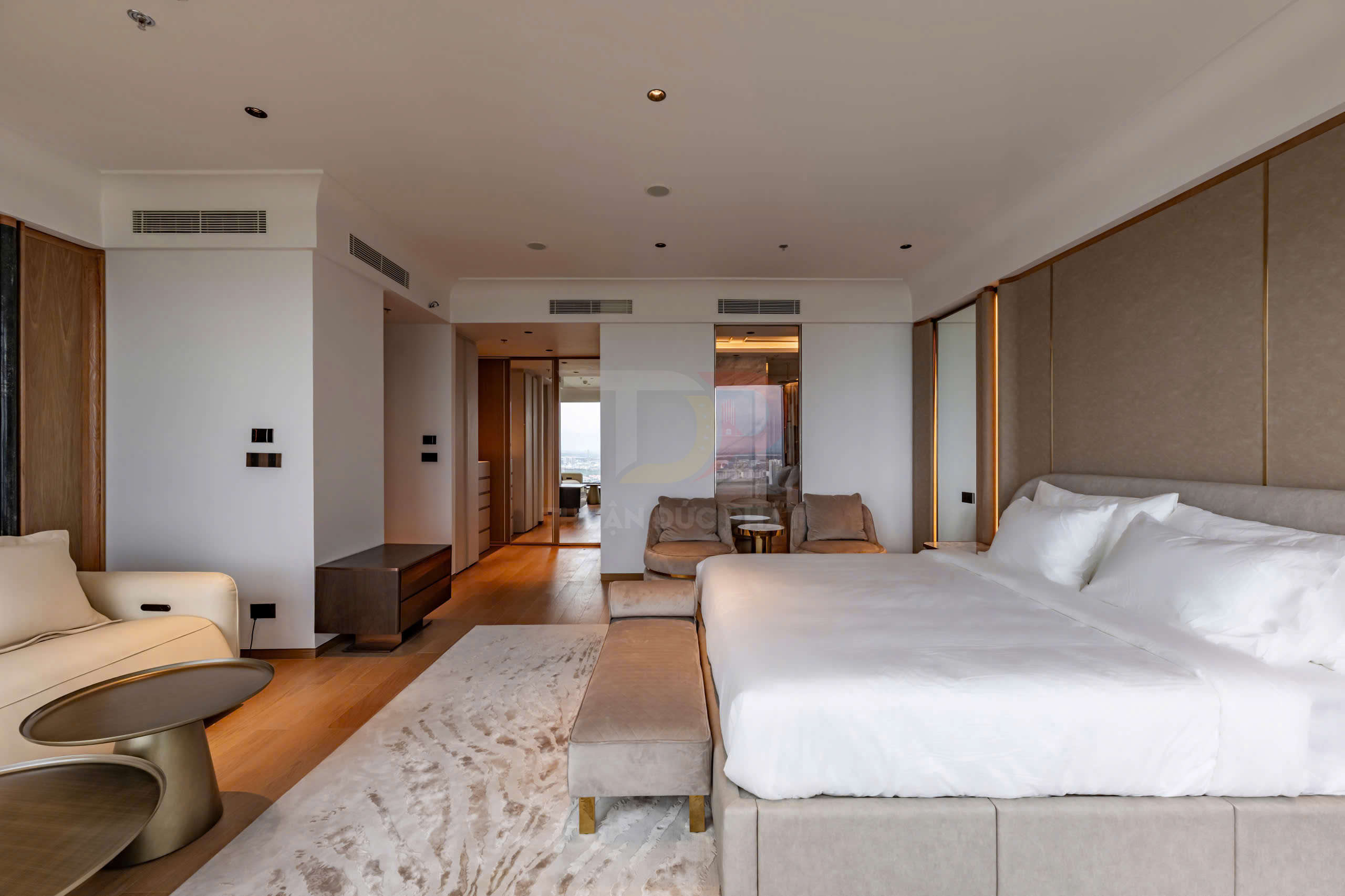 Phòng ngủ khách sạn cao cấp với giường đôi lớn, ghế sofa và nội thất hiện đại tông màu trung tính