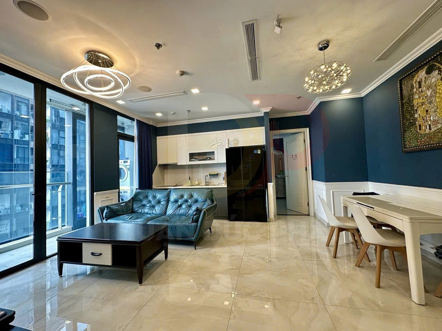 Phòng khách căn hộ hiện đại với sofa da xanh, bàn trà gỗ, bếp nhỏ và bàn ăn cạnh cửa kính lớn