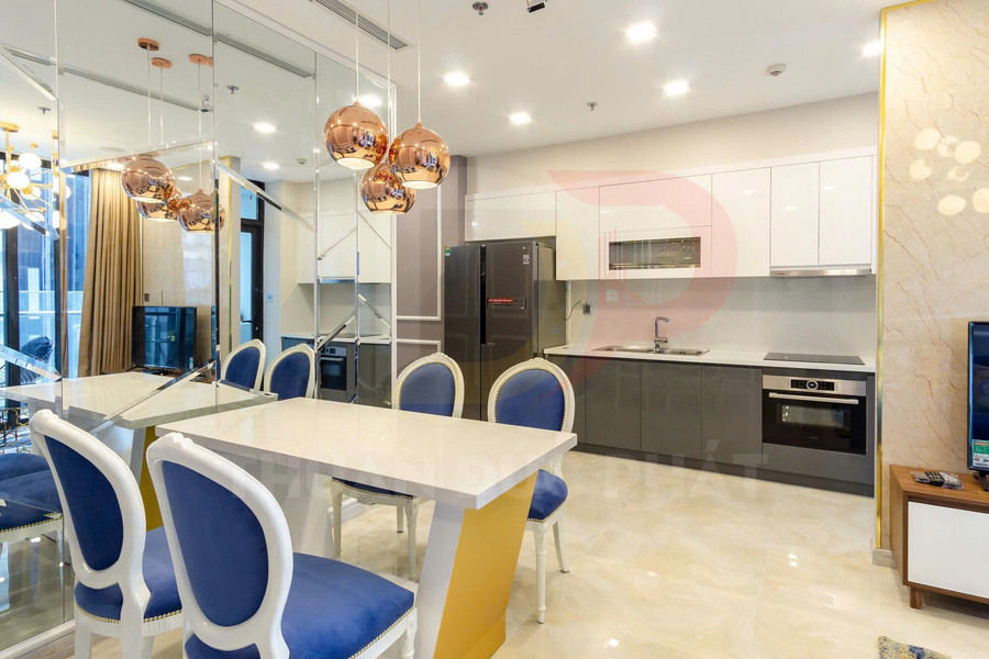 Bàn ăn hiện đại ghế nệm xanh cạnh tủ bếp chữ I và tủ lạnh lớn trong căn hộ cao cấp