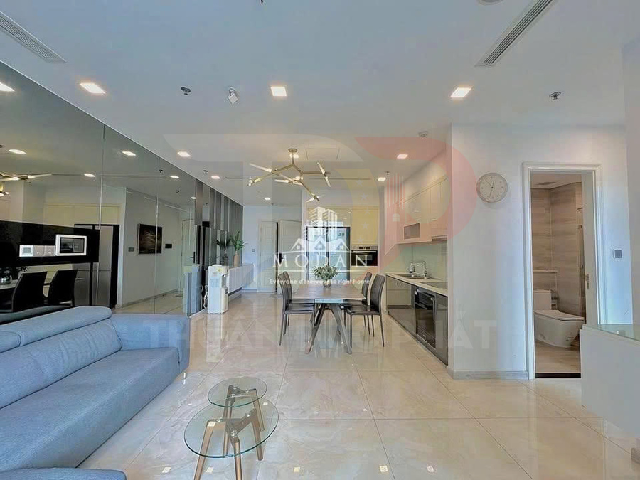 Phòng khách và bếp căn hộ hiện đại với sofa xám, bàn kính tròn và bộ bàn ăn cạnh tủ bếp sáng màu