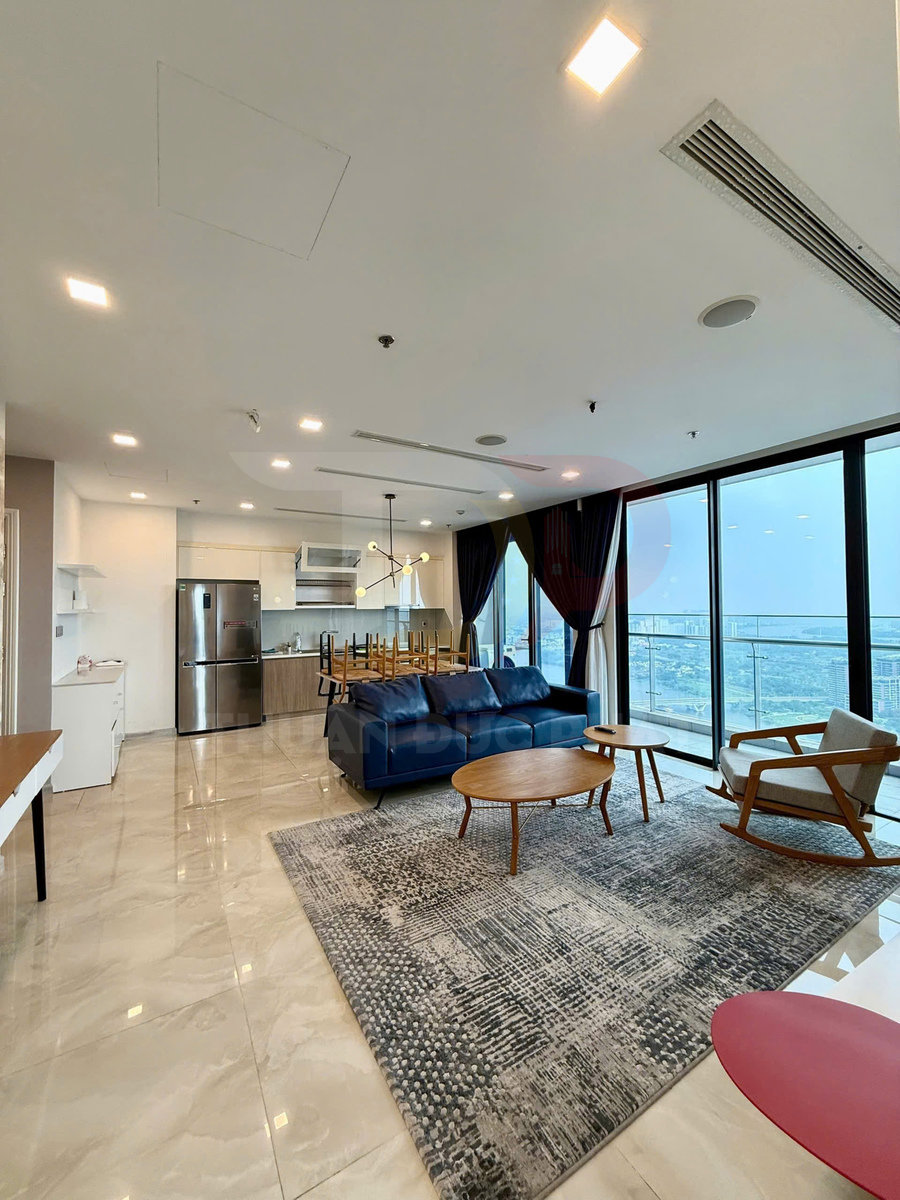 Phòng khách căn hộ hiện đại với sofa da xanh, bàn trà gỗ tròn và cửa kính lớn nhìn ra ban công