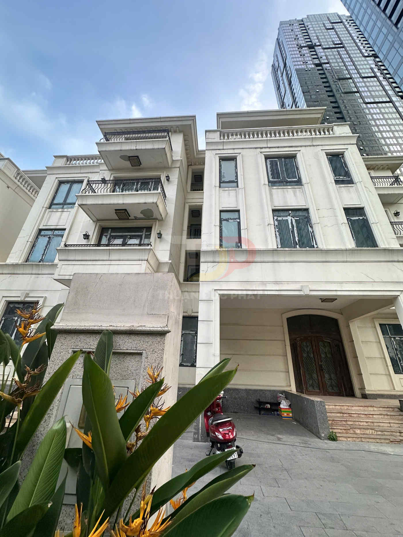 Mặt tiền biệt thự cao tầng màu trắng với ban công, cây cảnh và xe máy đỏ đỗ trước cửa