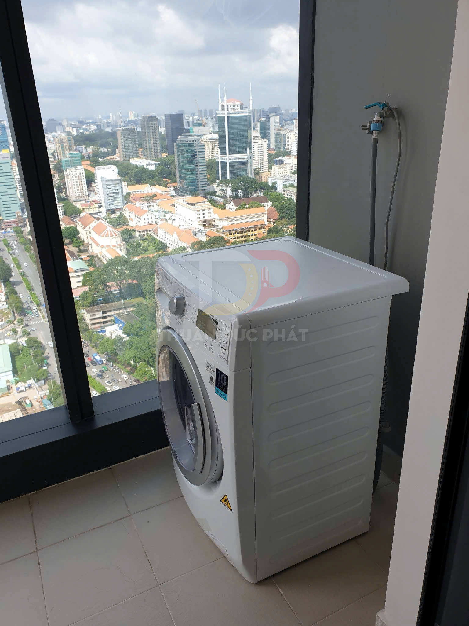 Máy giặt cửa trước màu trắng đặt cạnh cửa sổ căn hộ cao tầng nhìn ra thành phố
