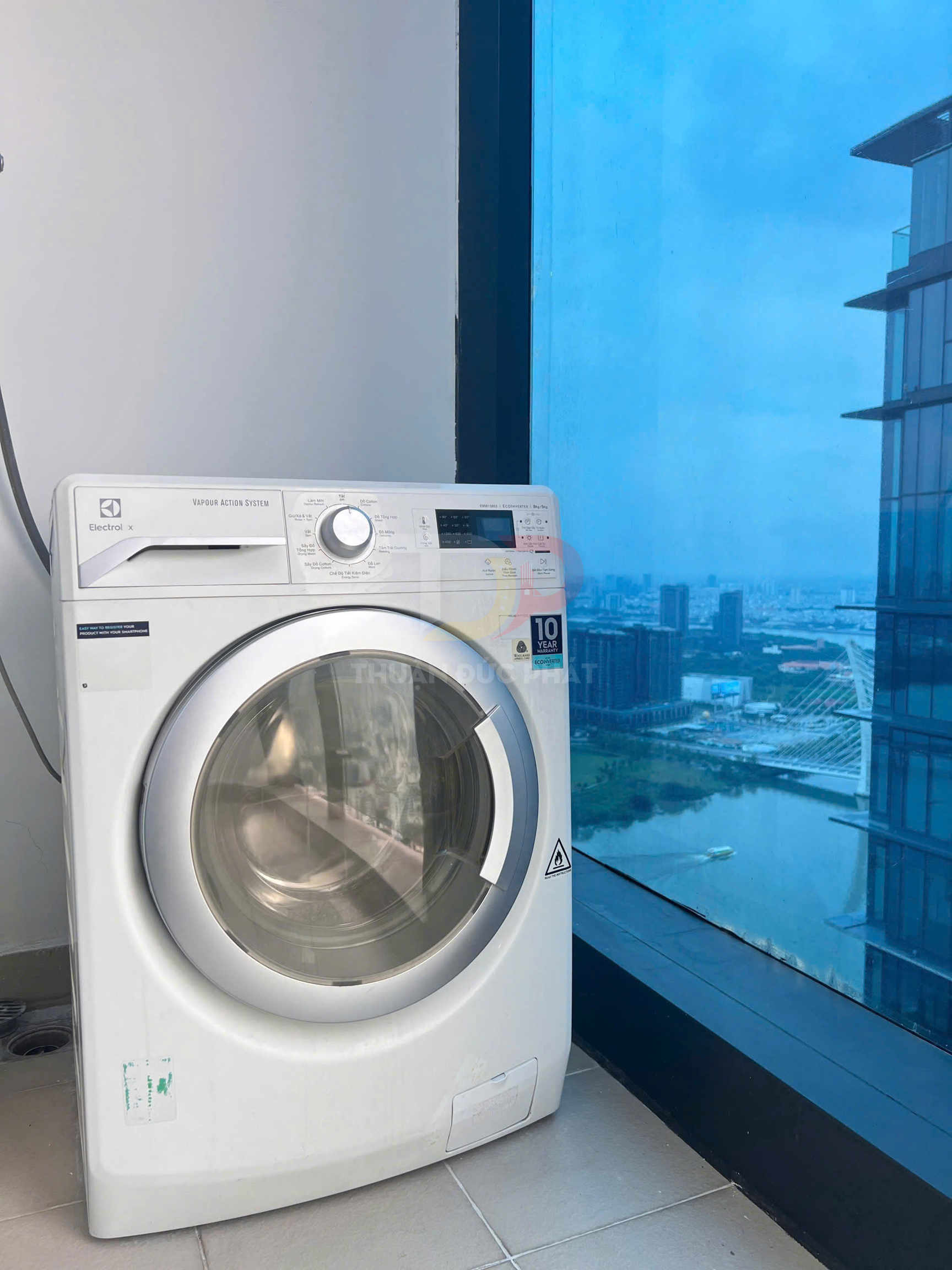 Máy giặt cửa trước Electrolux màu trắng đặt cạnh cửa sổ kính lớn trong căn hộ cao tầng
