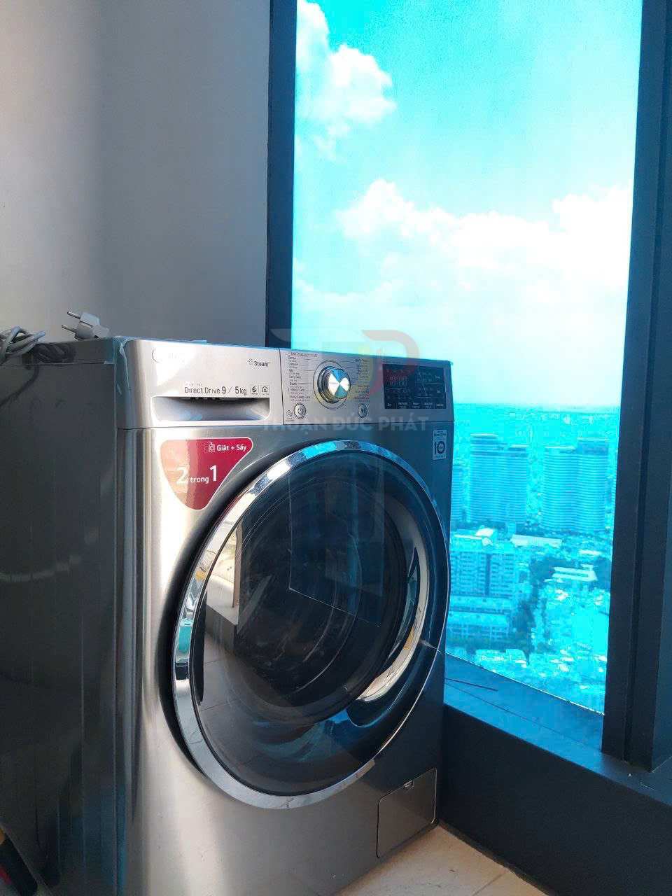 Máy giặt sấy LG cửa trước màu bạc đặt cạnh cửa sổ lớn nhìn ra thành phố