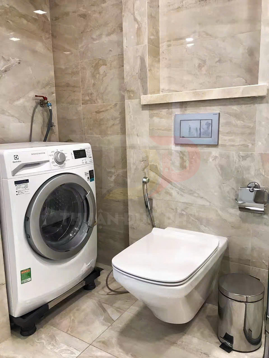 Máy giặt Electrolux đặt cạnh bồn cầu treo tường trong phòng tắm lát gạch sáng màu