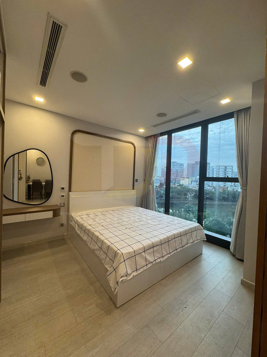 Phòng ngủ hiện đại với giường ngủ gỗ trắng ga kẻ caro cạnh cửa sổ kính lớn nhìn ra thành phố