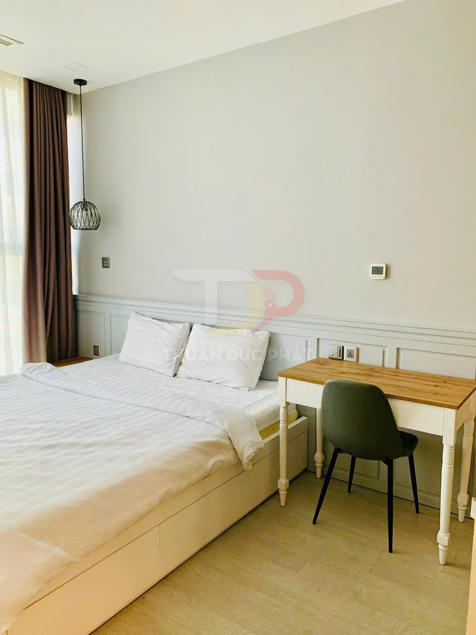 Phòng ngủ tối giản với giường ngủ trắng, ga gối trắng cạnh bàn làm việc gỗ và ghế nệm xanh